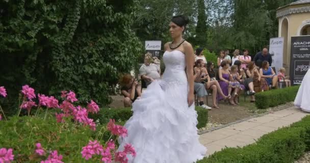 Жінки в білому сукні нареченої прогулянки по алеї з ніша вздовж рядків парад наречених глядачів в зелений парк старої старовинні будівлі квіти — стокове відео