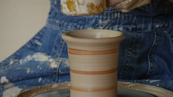 Potter ambachtsman in jeans is beglazing een pot door borstel roterende op aardewerk wiel gieten een klei pot vuile handen close-up gestreepte pot aardewerk workshop — Stockvideo