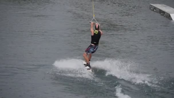 Лыжник в шлеме и купальнике катается на водных лыжах по направлению к Спрингборду Слайды по Спрингборду в Wake Park Green Sandy Bank — стоковое видео