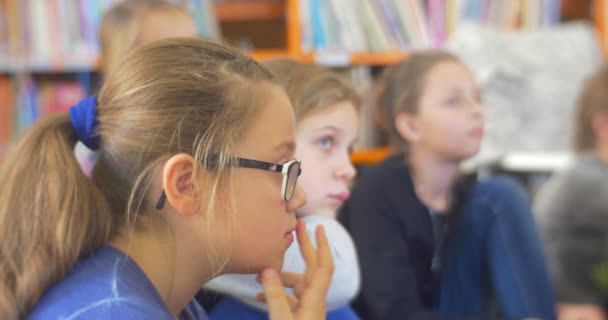 Група дітей діти дівчинки підлітки сидять на поверсі дивлячись в стійку з їх прослуховування для кого-то з серйозні обличчя в класі бібліотека — стокове відео