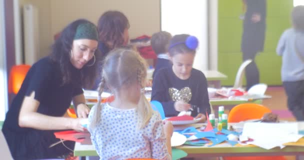 Los niños con sus educadores jóvenes están sentados haciendo un nuevo año apliques en la mesa ciervos hechos de papel muñeco de nieve hecho de placas de papel — Vídeo de stock