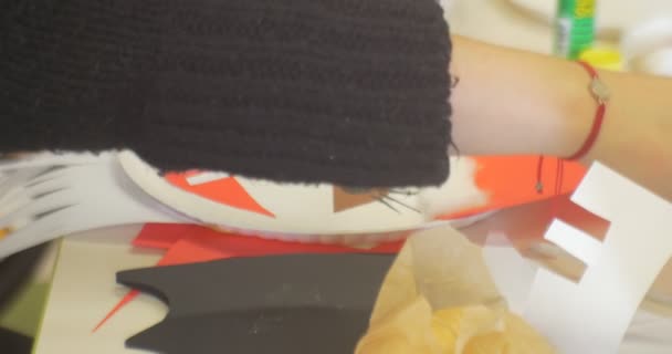 Mujer joven educadora en suéter negro Chica de mano femenina está haciendo una cara de papel de Año Nuevo apliques de un muñeco de nieve poniendo una lentejuelas al sombrero rojo del hombre — Vídeo de stock