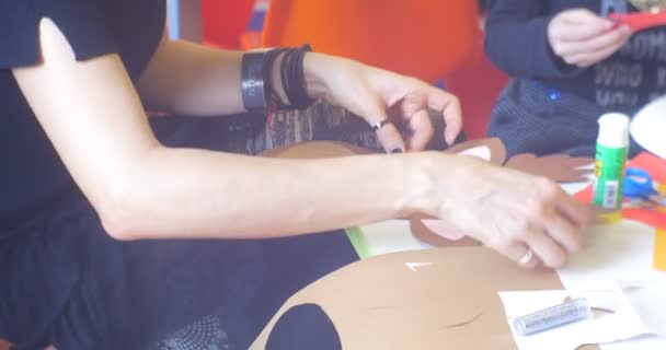 Подростки или молодые педагоги Женщина в черном делают новогоднюю аппликацию оленя за столом клея рога части аппликационного руки крупным планом — стоковое видео