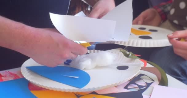 El hombre de las manos del educador está cortando un apliques de papel haciendo un muñeco de nieve Aplicaciones infantiles de placas desechables y apliques de papel de año nuevo — Vídeo de stock