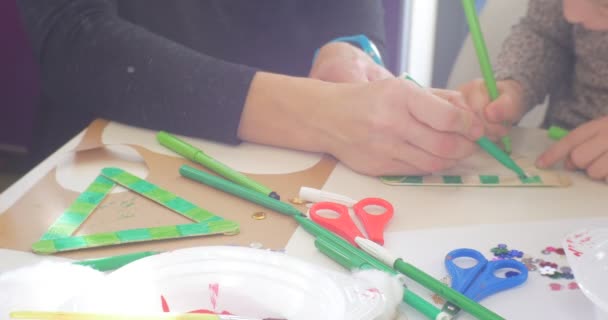 Los niños y el educador están coloreando un triángulo de juguete Marcador verde Las lentejuelas y las tijeras están en una mesa Las manos de cerca La gente está sentada a la mesa Pintura — Vídeo de stock