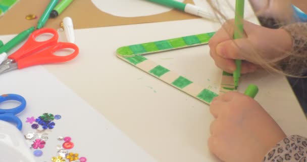 녹색 마커 스팽글로 삼각형을 색칠하는 아이의 손과 가위는 테이블 손에 가까이 아이가 테이블에 앉아 그림에 있습니다 — 비디오