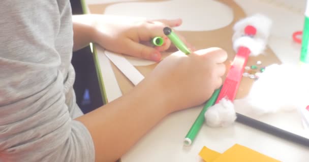 Mains d'enfant fille en chemisier gris peint Coloriage Triangle de décoration avec marqueur vert Peinture un jouet perles et paillettes sont sur la table — Video