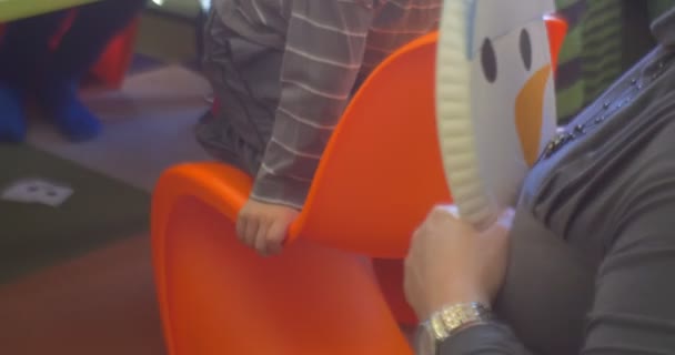 Opvoeder vrouw houdt een papier Snowman kinderachtig stoffen handen nauwe Up willen rechtzetten het Kids zitten op de oranje stoelen in een klaslokaal — Stockvideo