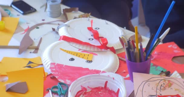 I bambini stanno facendo un pupazzo di neve di un piatto usa e getta matite Taglio carta vernici disordine su un tavolo Capodanno inverno Appliques in una classe della scuola materna — Video Stock