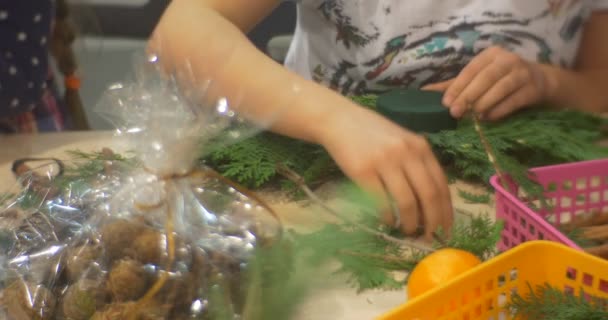 Fille rassemblant des branches pour créer une couronne Les gens font une composition de Noël des branches de couronne de l'Avent à la table Classe de maître du Nouvel An — Video