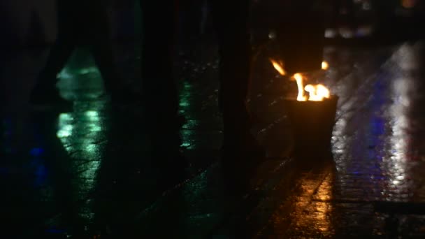 火在桶火舌头是上升舞者是走在火人的腿阴影人拿了一桶广场由五颜六色的灯 — 图库视频影像