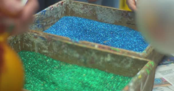 La main enfantine prend une poudre bleue de paillettes d'une boîte par cuillère pour décorer un jouet de Noël en verre Boîte à jouets en arbre du Nouvel An avec de la poudre verte de paillettes — Video