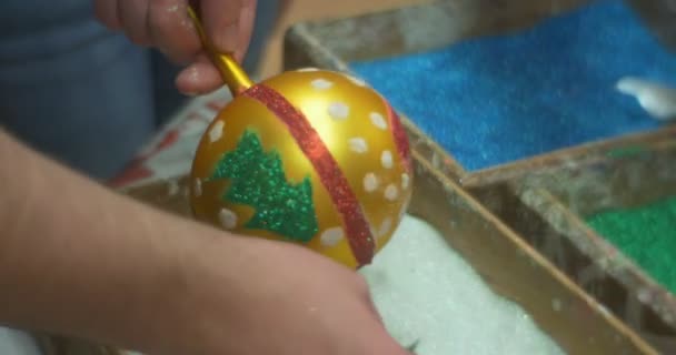 Руки наливают белый блеск порошок положить на желтый рождественский шар игрушки ложкой белые точки игрушки порошки остались на игрушки елка окрашена — стоковое видео