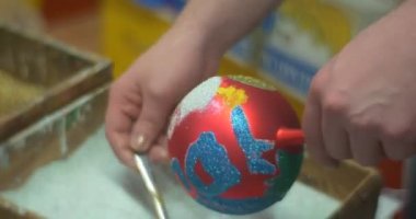 İnsanlar bir renkli pırıltılar tozu kaşık tarafından kendi gümüş ve kırmızı Noel topları için parlayan ve boyalı cam yeni yıl oyuncaklar sallayarak yağıyor