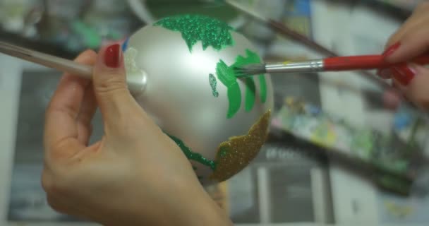 Női kéz a zöld festéket a kefével körmök egy nő egy ezüst karácsonyi bál festmény a festő a piros labda díszített csillogó Glitter — Stock videók