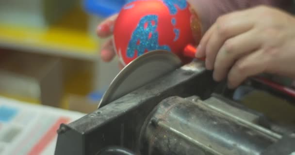 L'homme scie une poignée en verre d'un jouet de Noël rouge avant de donner le jouet à une personne qui l'a fait à la roue tournante de la classe de maître familiale — Video