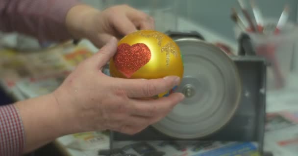 O punho de vidro dourado da bola é serrado para fora o homem da bola do brinquedo do Natal desliga uma máquina dá o brinquedo a uma pessoa que o fêz na classe mestre da família — Vídeo de Stock