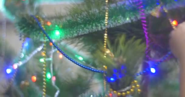 Девушка кладет разноцветные бусины в сосновое новогоднее дерево блестящие бусины и фонарики Sparking на зеленом дереве ветви девушка в серьги и корона — стоковое видео