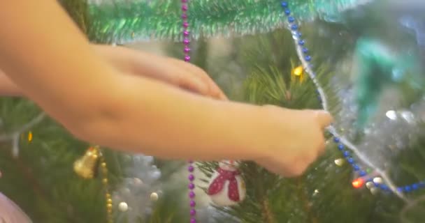Menina está colocando um boneco de neve de brinquedo para pinho decorado New-Year Tree Bell-Garlands e Lamplights coloridos Beads on a Branches Celebração da família em casa — Vídeo de Stock