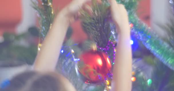 Девушка ставит красный рождественский бал украшенные новогодние елки сосны Белл-гирлянды и красочные фонари на ветках семейный праздник дома — стоковое видео