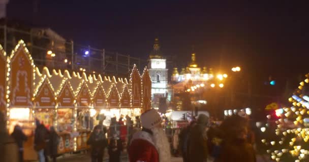Les gens sont aux kiosques de la foire de Noël à Sofia Square Santa Claus is Walking by the Square Lights Garlands Clock Tower New Year's Celebration Kiev Ukraine — Video