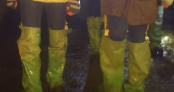 Nohy chůzi směrem k skupiny turistů v holínky je Walking podle proudu vody ve vodě v jeskyni je postřikování způsobem osvětlují lampy podzemní Kyjev — Stock video