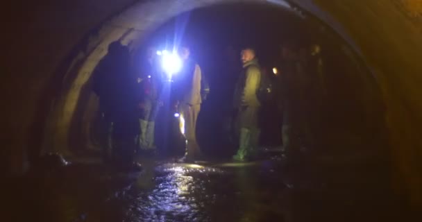 Tourists Observe The Cave Walls Light the Walls by Lamps Blind the Eye Semicircular Ceiling Small Water Stream under their Feet Underground River — Stock Video