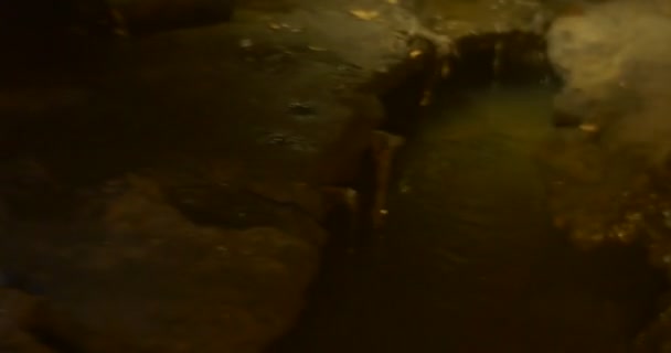 Turista se sienta sentada en cuclillas toma una foto de un arroyo río subterráneo en una cueva Dos personas caminan a lo largo de un río con botas de goma verdes iluminan el camino — Vídeo de stock
