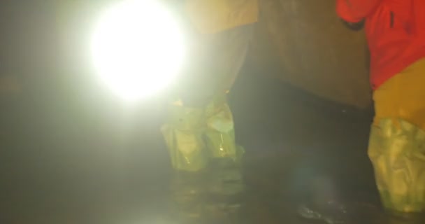 Mannen benaderingen van een oude pijp licht de buis knie-diepe ondergrondse rivier mannen zijn waden door water in een grot toeristen lopen zorgvuldig — Stockvideo