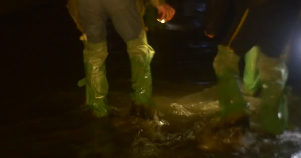 Touristen beleuchten ein Wasser an einer Lampe und erforschen einen kleinen Wasserlauf, der in grünen Gummistiefeln durch das Wasser watet. — Stockvideo