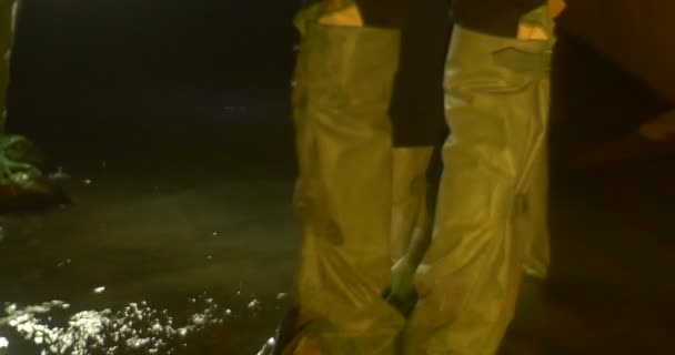 Mochileiros estão navegando cuidadosamente procurando lugar para fazer um passo turistas Rio-profundo do joelho em um grupo de caverna de homens em um Gumboots verde ilumina o caminho — Vídeo de Stock