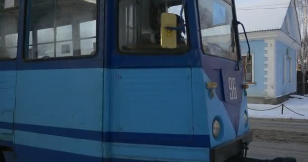 Personnes à l'intérieur du wagon de tramway bleu Piétons Les gens marchent par une rue Vieux tramway se déplace par un chemin de fer Bâtiments d'hiver Succursales nues Arbres — Video