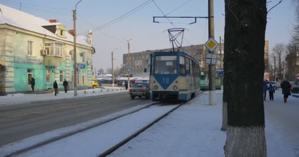 Lidé kráčí po ulici dvě tramvaje pohybující se na silnici žlutý autobus a auta na cestě zimní budovy holé větve stromy vánoční slunný den — Stock video