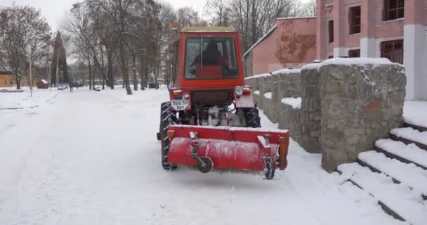 Ciągnik jest w ruchu do przodu wzdłuż budynku traktor czerwony spychacz jest sprzątanie parku aleja usuwa śnieg Central Park z Konotop nagie gałęzie drzewa — Wideo stockowe