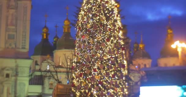 Persone che camminano all'albero di abete illuminato Stella splendente sull'albero di Capodanno decorato con ghirlande di lampade Cupole d'oro del video della Chiesa sullo schermo TV Kiev — Video Stock