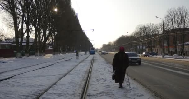 Mulher com bengala caminha ao longo da estrada carros estão deixando as árvores velhas ferroviária ao longo da rua neve na terra Mir Avenida na cidade de Konotop — Vídeo de Stock