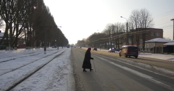 Жінка з за тростиною перетинає вулицю автомобілі є рушійною на залізничні старих дерев уздовж вулиці сніг на землі мир-авеню в місті Конотоп — стокове відео