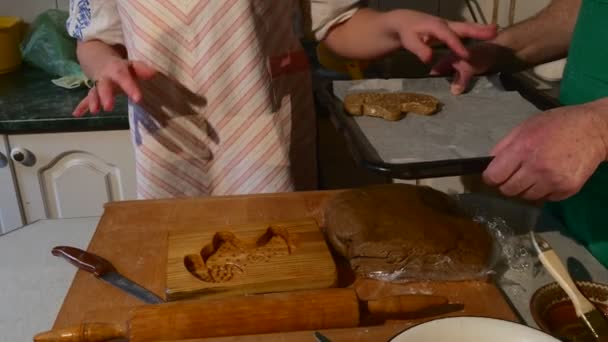 Vrouw toont ruimte op bakken lade Cookie is geplaatst op een lade man in Green schort houdt een lade en de familie van de vrouw is Making Ram-Shaped Cookies — Stockvideo