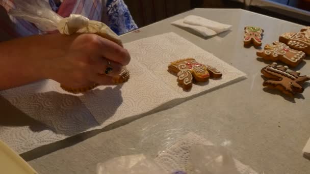 Mulher está pintando um coração-biscoito com biscoitos de Natal de mastique branco decorado com mastique em uma mesa na frente da mulher botões de chocolate — Vídeo de Stock