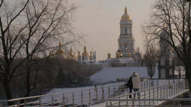 Deux filles sont debout sur un pont Wintery Park Les adolescents regardent l'écran de la caméra regardant des photos qui vont prendre une photo Cathédrale de Kiev Towers — Video