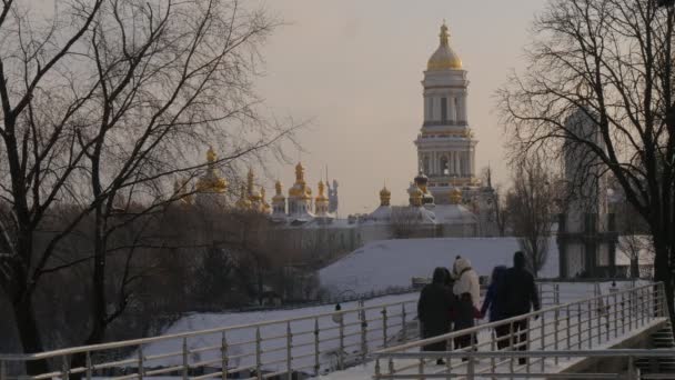 Οικογένεια παιδιά γονείς Wintery πάρκο άνθρωποι περπάτημα από γέφυρα δύο νεαρά κορίτσια είναι στέκεται πάνω από μια γέφυρα και πρόκειται να λάβει μια φωτογραφία Κίεβο πύργους καθεδρικός ναός — Αρχείο Βίντεο
