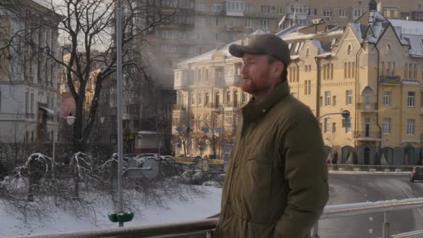 Человек нажимает на кнопки на мобильном телефоне, стоящем на мосту Зимний пар выходит из рта Винтажный Браун-Блокированный строитель думает городской пейзаж — стоковое видео