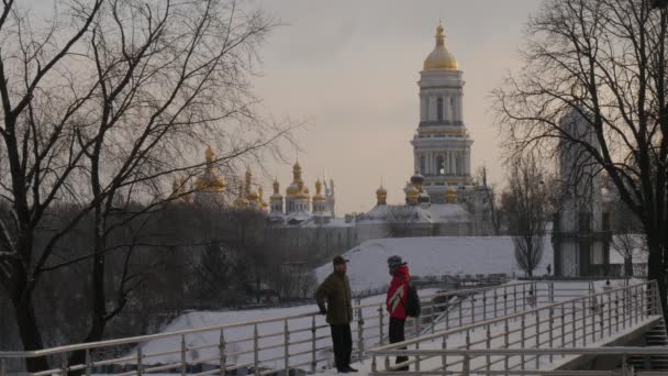 2 人の男性の友人父息子は地平線上のウィンターパーク黄金のドーム ベル Kievo タワー Pecherskaya Lavra を離れて歩く歩道橋ジロード — ストック動画