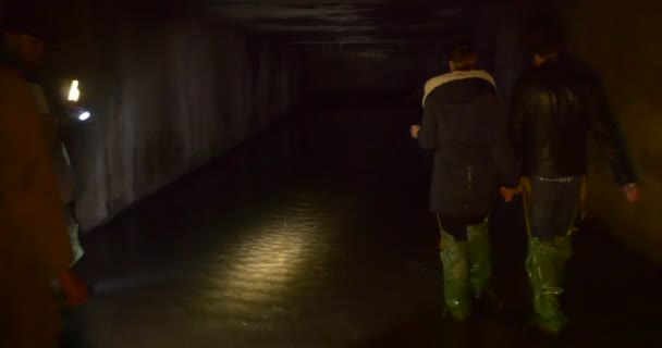 Fyra personer är på väg mot en grotta ljus vägen av ljus manliga och kvinnliga turister i gröna Gumboots i en mörk grotta Kiev underjordiska floder — Stockvideo