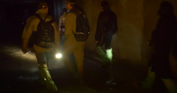 Велосипедисты идут вперед по Подземным водам Люди в зеленых резиновых сапогах освещают путь со светлыми туристами в темной пещере Киева — стоковое видео