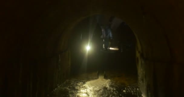 Man Lights strumień wody półokrągły sufit w jaskini turystów w ciemnej jaskini w nowym roku wycieczka do Kijowa Underground ludzie światło drogę — Wideo stockowe