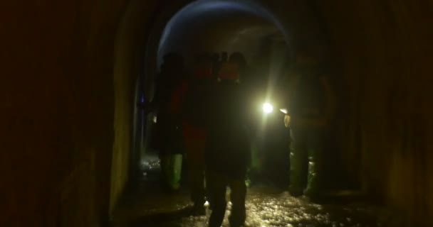 Silhouetten von Menschen spazieren an einer Wand entlang Wassertouristen in einer dunklen Höhle in Gummistiefeln beim Neujahrsausflug zu Kiewer U-Bahn-Leuten beleuchten den Weg — Stockvideo