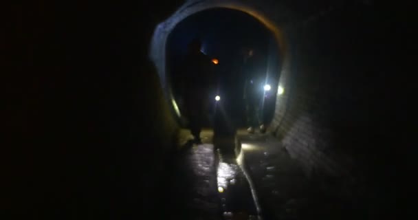 Turistas estão caminhando ao longo da luz do túnel escuro o caminho por lâmpadas andando ao longo de paredes de um túnel estreito Excursão de Ano Novo para rios Kiev subterrâneos — Vídeo de Stock