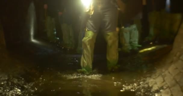 Hombre con botas de goma caminando por separado por el grupo de agua es Turistas de pie en una luz oscura cueva El camino por las lámparas Excursión de Año Nuevo al metro de Kiev — Vídeos de Stock