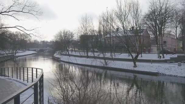 Панорама парка медленного движения на набережной Тихий район города Высокие деревья и дома рядом с маленькой рекой Снег на наземный зимний день — стоковое видео